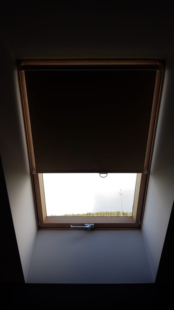 Okno dachowe do połowy zasłonięte tkaniną zaciemniającą 